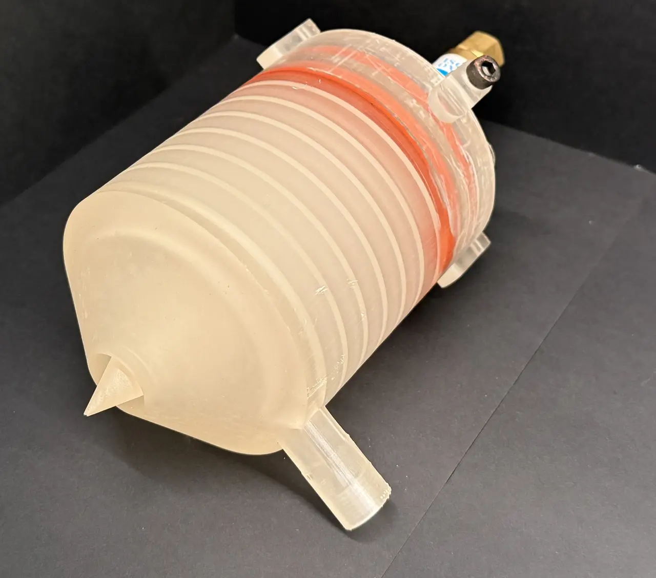 Translucent ribbed resin engine body seen from the nozzle end with the pointed spike in the foreground and a brass fitting at the far end