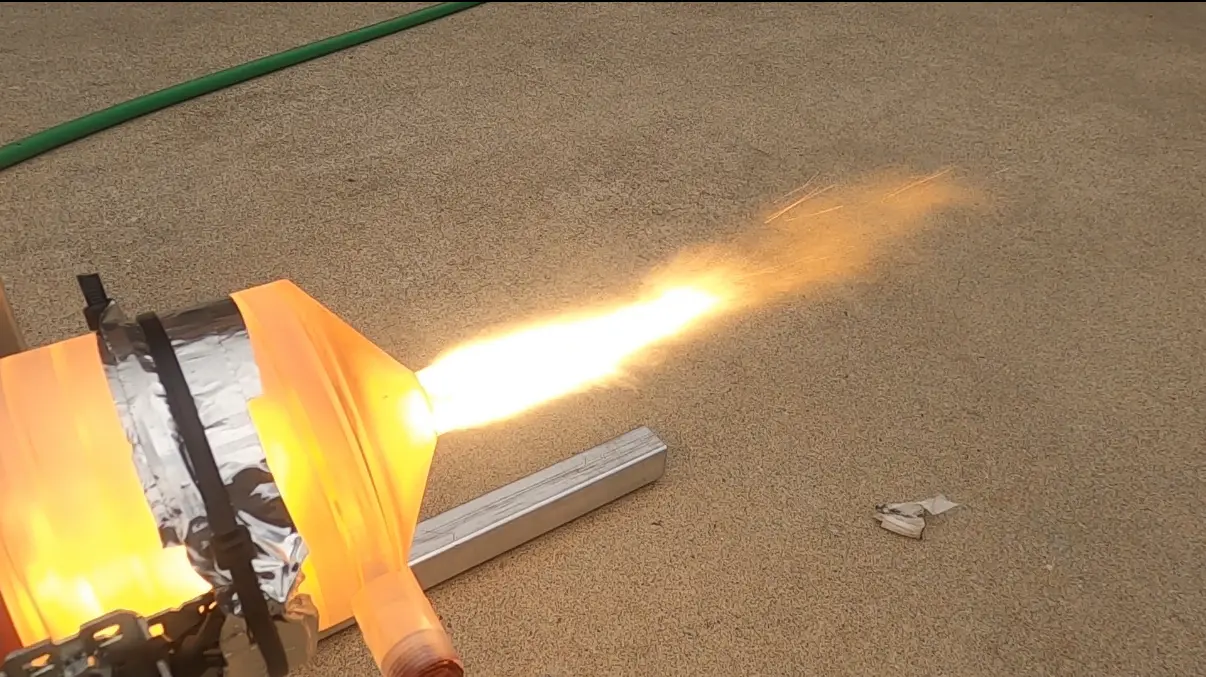 Bright orange exhaust plume leaving the foil-wrapped Version 3 aerospike engine over a tan floor during a hot-fire test
